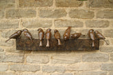 Bronze sculpture of birds on a sculptural form on a stone wall