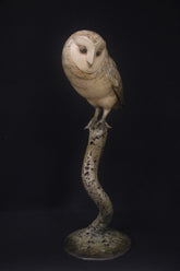 Statue of an owl perched on a branch against a black background