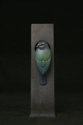 Decorative bird sculpture on a dark pedestal against a black background