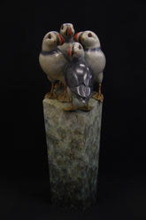 Bronze sculpture of four puffins gathered together on green patina ledge.