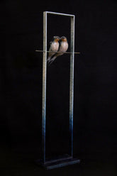 Bronze sculpture of two birds perched on a metal stand against a black background