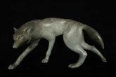 Bronze sculpture of grey wolf walking against a black background.