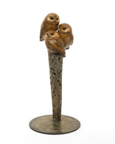Bronze sculpture of three owls on a branch with a white background