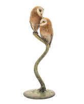 Bronze sculpture of two owls perched on a curved branch on a white background