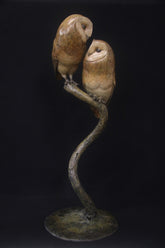 Bronze sculpture of two owls perched on a branch against a black background