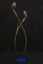 Bronze sculpture of two kingfisher birds on a plant-like structure against a dark background