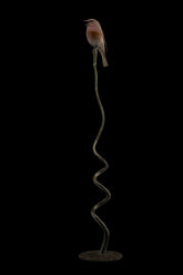 Bronze sculpture of bird perched on a long, thin branch against a black background