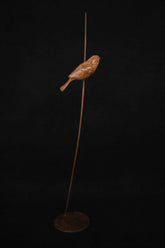 Bronze sculpture of small bird perched on a thin branch against a dark background