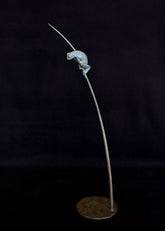 Bronze sculpture of a tree frog on a branch against a black background