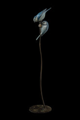Bronze sculpture of two blue birds on a branch with a black background