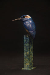 Blue bird bronze sculpture on a green and brown pedestal against a black background