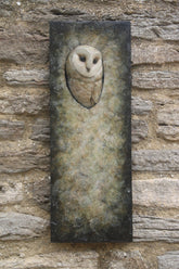 A rectangular stone wall plaque featuring a carved or sculpted barn owl head set into a textured, weathered stone background, mounted on a rustic stone wall.