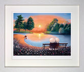 Framed artwork of a couple on a bench by a lake at sunset.