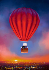 Red hot air balloon floating above a cityscape at sunset.