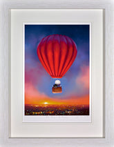 Framed artwork of a red hot air balloon over a cityscape at sunset.