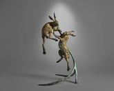 Bronze sculpture of two animals in mid-air on a gray background
