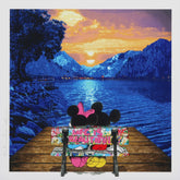 Two cartoon characters sitting on a bench by a lake with mountains at sunset.