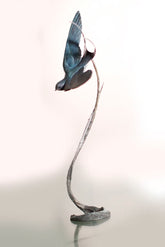 Bronze sculpture of a bird perched on a branch against a white background