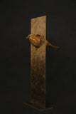 Bronze sculpture of a bird on a vertical rectangular base against a black background