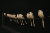 Row of bronze sculpture birds on a wire against a black background