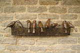 Bronze sculpture of birds on a sculptural form on a stone wall