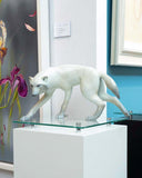 White walking wolf on a white glass stand against colourful artwork