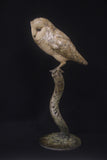 Bronze owl sculpture on a branch against a black background