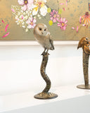 Bronze sculpture of barn owl on a curved branch against a floral artwork
