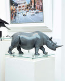Bronze rhinoceros sculpture on a glass platform with a cityscape painting in the background