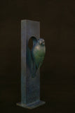 Decorative bird sculpture on a rectangular stand against a dark background