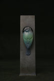 Decorative bird sculpture on a dark pedestal against a black background