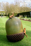 Large sculpture of an acorn with two small squirrels on top, set against a garden backdrop.