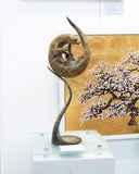 Bronze sculpture of an otter on a glass pedestal with a cherry blossom painting in the background.