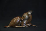 Bronze sculpture of a deer lying down on a black background