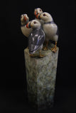 Bronze sculpture of four puffins gathered together on green patina ledge.