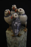 Bronze sculpture of four puffins gathered together on green patina ledge.