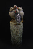 Bronze sculpture of four puffins gathered together on green patina ledge.