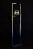 Bronze sculpture of two birds perched on a metal stand against a black background