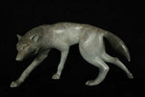 Bronze sculpture of grey wolf walking against a black background.