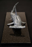 Bronze sculpture of a shark on a granite base and dark background