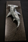 Bronze sculpture of a shark on a granite base and dark background