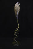 Bronze sculpture of a kestrel perched on a twisted base against a black background