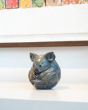bronze sculpture of grey koala on a white table behind a colourful artwork