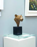 Bronze sculpture of a leopard head on a black cube pedestal in an art gallery.