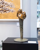 three small bronze owls perched on a branch sculpture on a plinth in gallery
