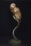 Bronze sculpture of two owls perched on a branch against a black background
