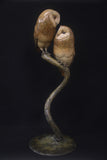 Bronze sculpture of two owls perched on a branch against a black background