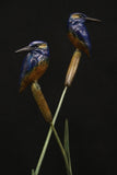 Bronze sculpture of two kingfisher birds on a plant-like structure against a dark background