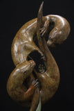 Bronze sculpture of two otters interacting with a fish on a black background
