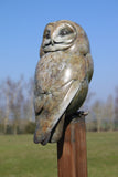Bronze sculpture of an owl on a tall pole in a garden setting